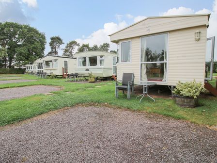 Several caravan homes with outdoor chairs and tables on grass and gravel at 1 Old Orchard in Brockton near Much Wenlock