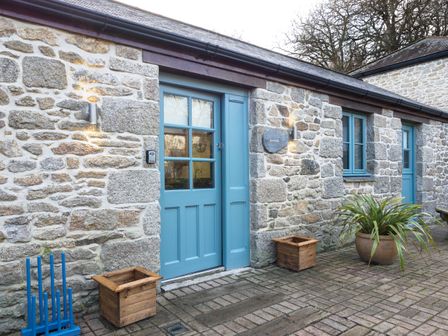 A stone exterior wall with two blue doors windows and planters at Manacles in Mawnan Smith Near Falmouth