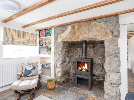 A stone fireplace with a black wood-burning stove and a reading chair with a footrest near a window at Isfryn Llanengan near Abersoch