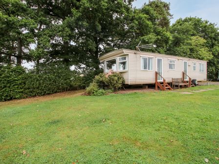 A mobile home with steps and bench outside surrounded by grass and trees at 7 Old Orchard in Brockton near Much Wenlock