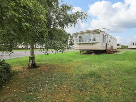 A caravan on a grassy area near a tree and a gravel path at 8 Old Orchard in Brockton near Much Wenlock