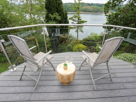 Two chairs and a small table with glasses on a balcony overlooking a river and trees at Ynys Castell in Menai Bridge