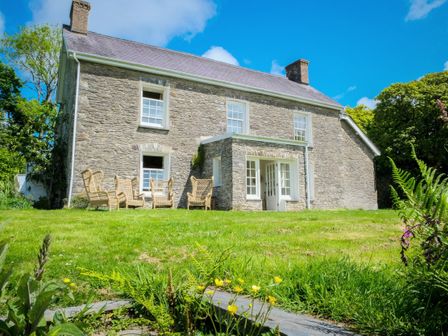 Stone house with lawn and outdoor wicker chairs at Henllys Newport Pembrokeshire