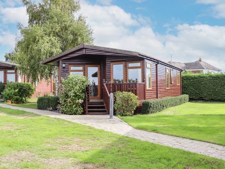 An exterior view of a wooden cabin with a small porch and surrounding grass at Lodge Two Country View Park in Graveney