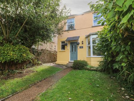 Front yard with pathway leading to a blue door on a two story yellow house surrounded by trees and bushes at Greengate in Tenby