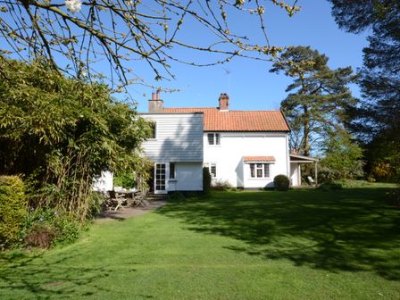 A white house with a red tiled roof surrounded by a green lawn and trees at Durdans Walberswick in Walberswick