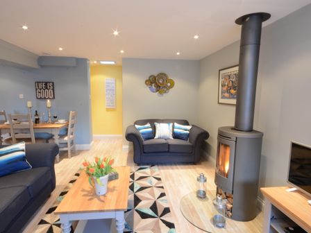 A living room with two blue sofas a wooden coffee table with flowers a wood stove and a dining table at Bunny Cottage Aldeburgh