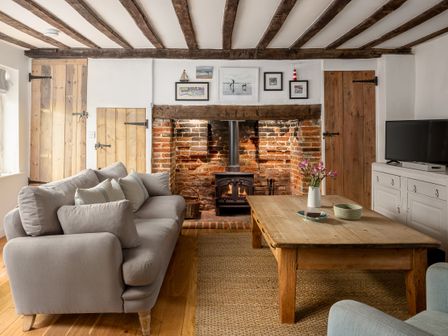 A living room with a gray sofa a wooden coffee table flowers on the table a brick fireplace and wooden doors at 7 Church Street Southwold