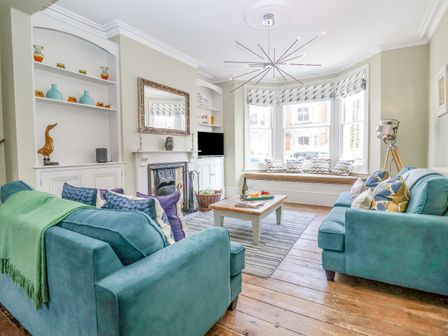 A living room with blue sofas a coffee table and bay window seating at Heron House Southwold