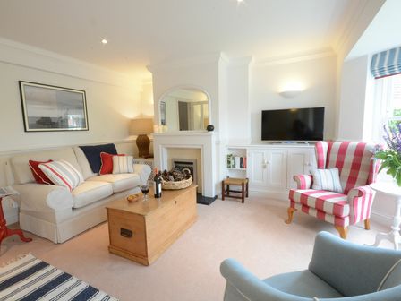 A living room with a sofa cushions a wooden chest a television and armchairs at Nutmeg Aldeburgh in Aldeburgh