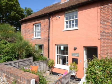 The exterior of a brick and painted cottage with a garden bench and potted plants at 6 Coastguard Cottages Aldeburgh