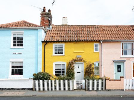 A row of three houses with blue yellow and pink exteriors and white picket fences at Aldeburgh Cottage in Aldeburgh