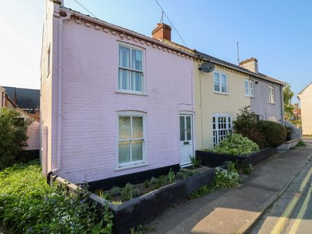 A row of three terraced houses painted pink yellow and gray with small garden beds in front at Mariners Cottage in Aldeburgh