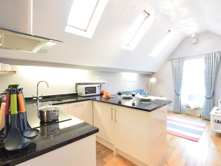 A kitchen with black countertops a microwave sink and cooking utensils next to a small sitting area with a rug and chair at Pied a Mer Aldeburgh