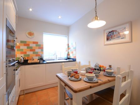 A kitchen with a wooden table set for breakfast and colorful tiled backsplash at The Hideaway in Aldeburgh