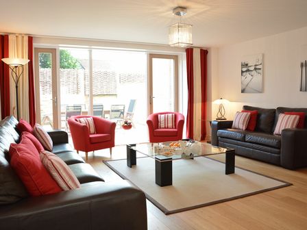 A living room with brown leather sofas red armchairs a glass coffee table and large windows at The Shelduck Southwold