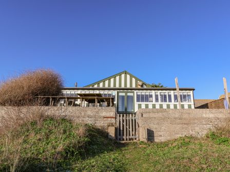 A house with green and white striped facade behind a concrete wall and gate at Valetta Thorpeness in Thorpeness