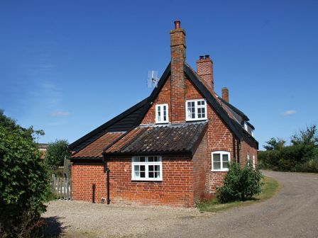 A brick house with white windows and multiple chimneys on a gravel driveway at 1 Grange Cottages Westleton