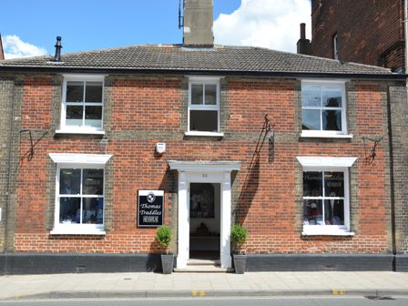 A brick building with a menswear shop named Thomas Traddles with windows and a doorway at Southwold Arms Apartment in Southwold