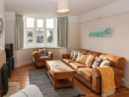 A living room with brown leather sofa and armchair wooden coffee table and bay windows at Sailors Rest Southwold