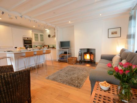 An open-plan living room and kitchen with a sofa a fireplace a TV and a kitchen island with bar stools at Vesta Cottage Orford