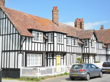 A row of black and white Tudor style houses with a yellow door and cars parked outside at 4 The Dunes Thorpeness