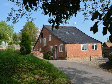 A brick house with a black tiled roof and multiple windows surrounded by trees and grass at 1 The Old Coach House Huntingfield Near Laxfield