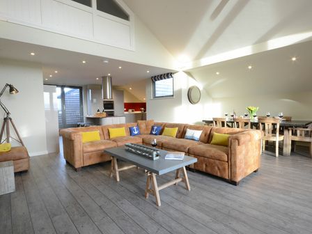 An open living room with a large brown sectional sofa and a wooden dining table with chairs at King George Penthouse in Aldeburgh