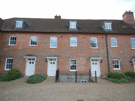 A row of brick townhouses with white doors and windows with small garden shrubs in front at Saffron Blythview in Blythburgh near Southwold