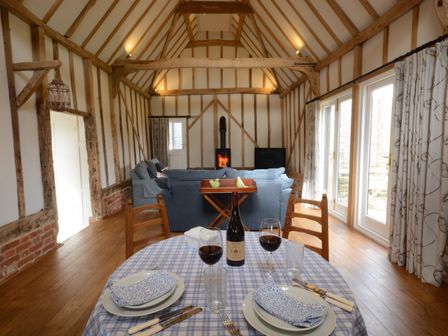 A dining table set with plates glasses and wine in a room with wooden beams blue sofas wood floor and a fireplace at Bird Cottage Burgh Near Grundisburgh