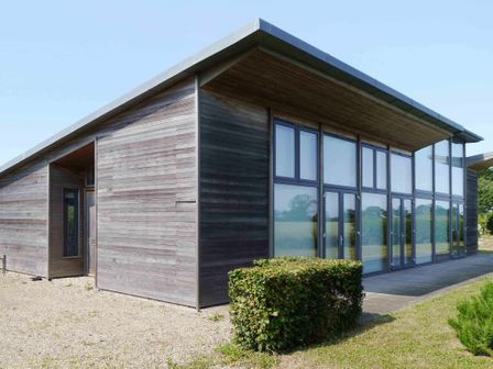 An exterior view of a modern wooden house with large windows and a hedge in front at Upper Lodge Shotley