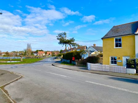 A street with houses trees a pond and a yellow house with a white fence at 1 South Cottages in Thorpeness