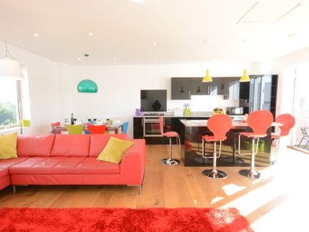 An open plan living room and kitchen with a red sofa and yellow pillows at Parrotfish Bay in Southwold