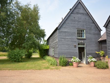 An exterior view of a wooden house with potted plants near the door and trees on a grassy area at The Gig House Stowupland