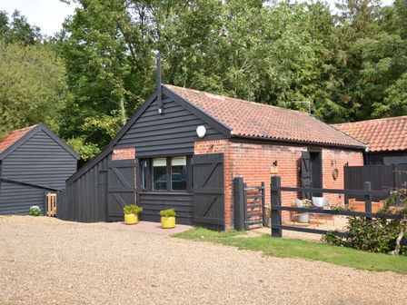 A small brick and wood building with a tiled roof and two yellow plant pots outside at Milk Parlour Spexhall Near Halesworth