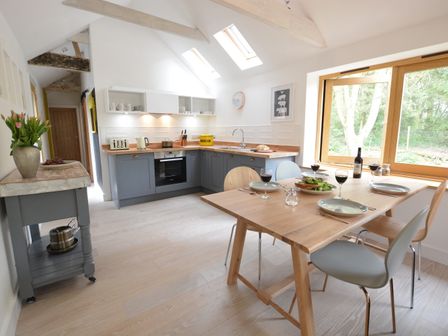 A kitchen with a wooden dining table set for four and gray cabinets under skylights at Red Poll Barn Spexhall Near Halesworth