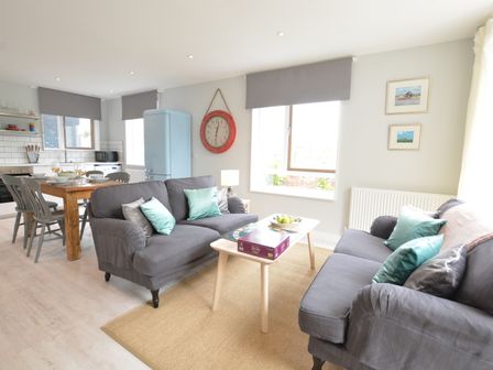 A living room with gray sofas and a wooden dining table at Sweet Pea Southwold