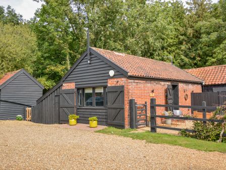 A small brick and wood outbuilding with a tiled roof and outdoor seating area at Spexhall Barns in Halesworth