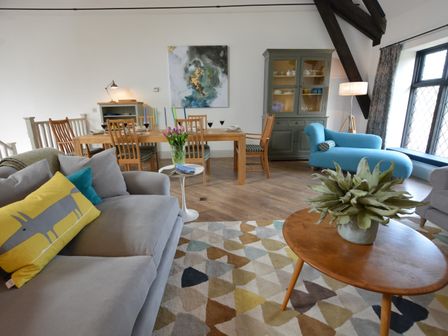 A living room with a gray sofa a wooden dining table with chairs a blue chaise lounge and a wooden coffee table with a plant at Badminton Thorpeness in Thorpeness