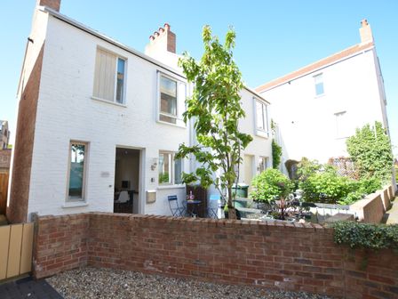 A white brick house with windows a small garden a tree and outdoor chairs at Mycroft Southwold in Southwold