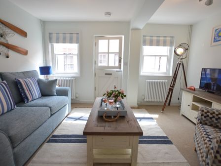 A living room with a blue sofa striped cushions coffee table and television at Alinka Aldeburgh in Aldeburgh