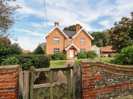 A brick house with decorative white trim and a garden behind a wooden gate at Church Farm Dunwich Near Westleton