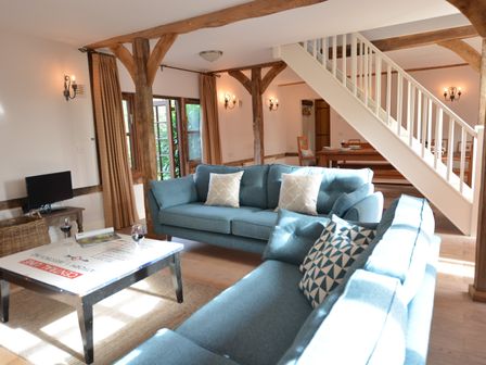 A living room with blue sofas a coffee table wine glasses and wooden beams at Wheelwrights Barn in Walpole Near Halesworth