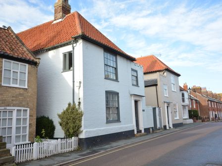 A street with white and brick houses with red tile roofs and small trees along the sidewalk at Gosfield Cottage Aldeburgh