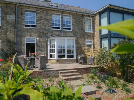 A brick house with a patio and outdoor seating area with plants in the garden at 10 Church Walk Aldeburgh