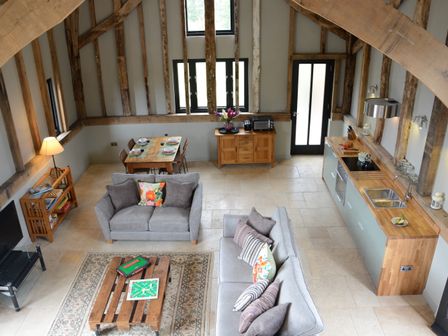An open living space with two sofas a wooden coffee table a dining table a kitchen area and exposed wooden beams at Manor House Barn Peasenhall