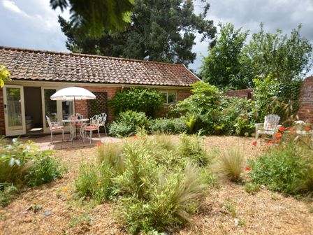 A garden with plants gravel and patio furniture in front of a brick building with tiled roof at The Nookery at Snape Hall in Snape Suffolk