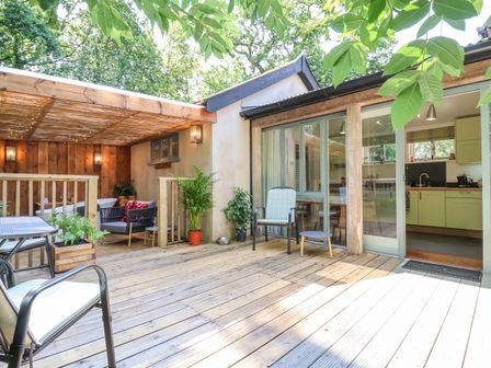 An outdoor wooden deck with chairs tables potted plants and a partially covered sitting area next to a kitchen at Yew Tree Farm Stable Worlingworth