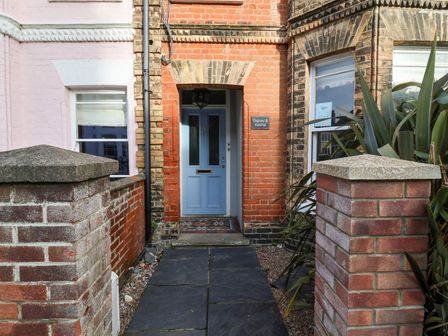 A blue front door set in a brick facade with a tiled doorstep and plants on the side at Kestrel and Osprey in Southwold