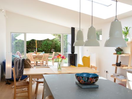 A dining room with wooden furniture and a vase with flowers next to a kitchen island with a bowl at 2 Pink Cottages Aldeburgh